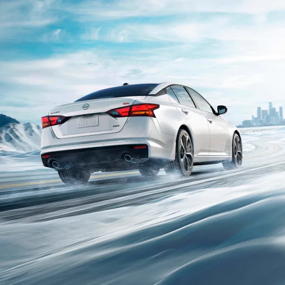 2027 Nissan Altima in white seen from behind driving in snowy landscape illustrating all-wheel drive at Ricart Nissan in Groveport OH